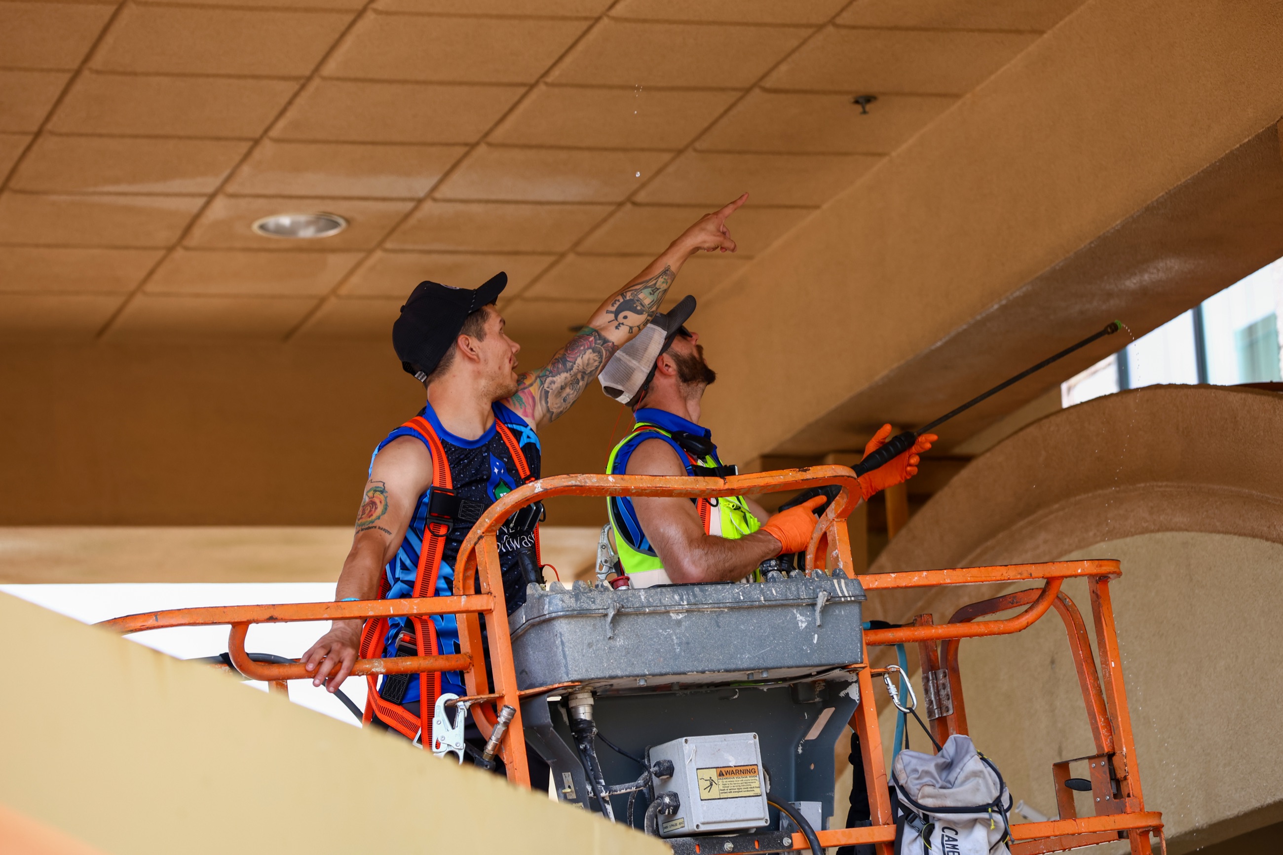 NETX Softwash crew in harnesses inspecting and cleaning a hotel soffit from a boom lift